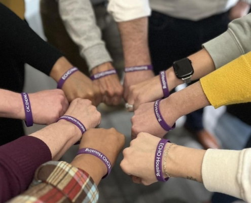 Arms and hands in a huddle with purple bracelets