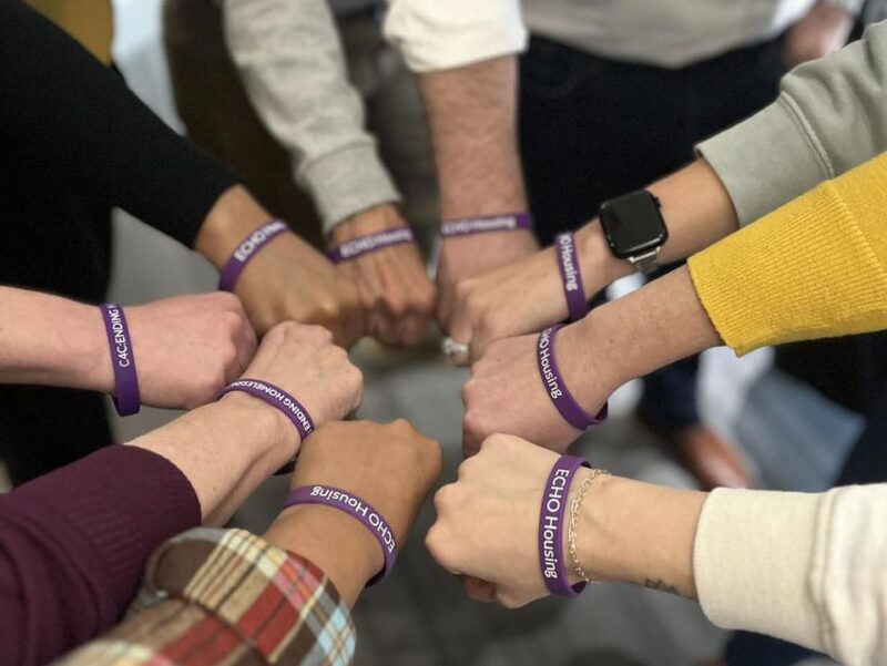 Arms and hands in a huddle with purple bracelets